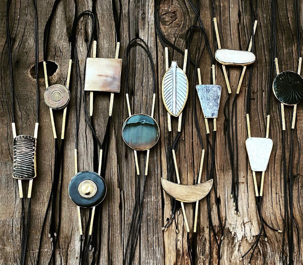 # Boho Pendant Necklaces with Natural and Ceramic Elements

This collection of handcrafted pendant necklaces features an eclectic bohemian aesthetic with mixed materials including ceramic, metal, and natural wood accents, likely from the contemporary artisan or vintage 1970s-2000s era. The pieces showcase earthy tones of white, cream, blue, and black combined with metallic findings and leather or cord stringing, with distinctive elements such as leaf-shaped pendants, circular ceramic medallions, striped patterns, and textured surfaces. Notable features include the varied pendant shapes ranging from geometric to organic forms, the use of natural raw materials, and the hand-assembled quality typical of boho or ethnic-inspired jewelry design.