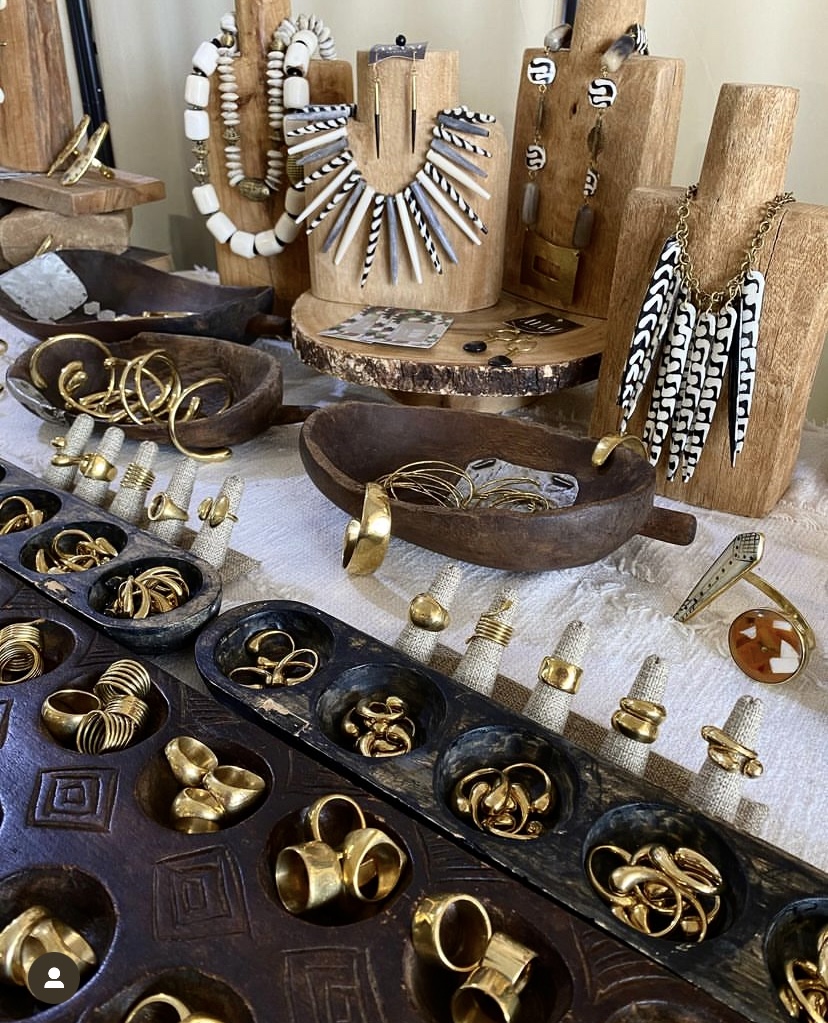 # Jewelry Display and Storage Set

This is a handcrafted wooden jewelry display and organization system featuring natural wood stands, carved display busts, and dark wood trays, likely from the 1970s-1980s bohemian or artisan era. The set includes multiple wooden display stands in light natural wood tones, carved wooden jewelry busts with decorative elements, and dark stained wood organizer trays with compartments, complemented by cream linen display blocks and brass fixtures. Notable features include hand-carved details on the busts, woven rope accents on some necklace displays, a collection of brass and gold-toned rings and bangles organized in divided trays, and white and black beaded necklaces, representing a complete vintage jewelry merchandising or personal collection presentation system.